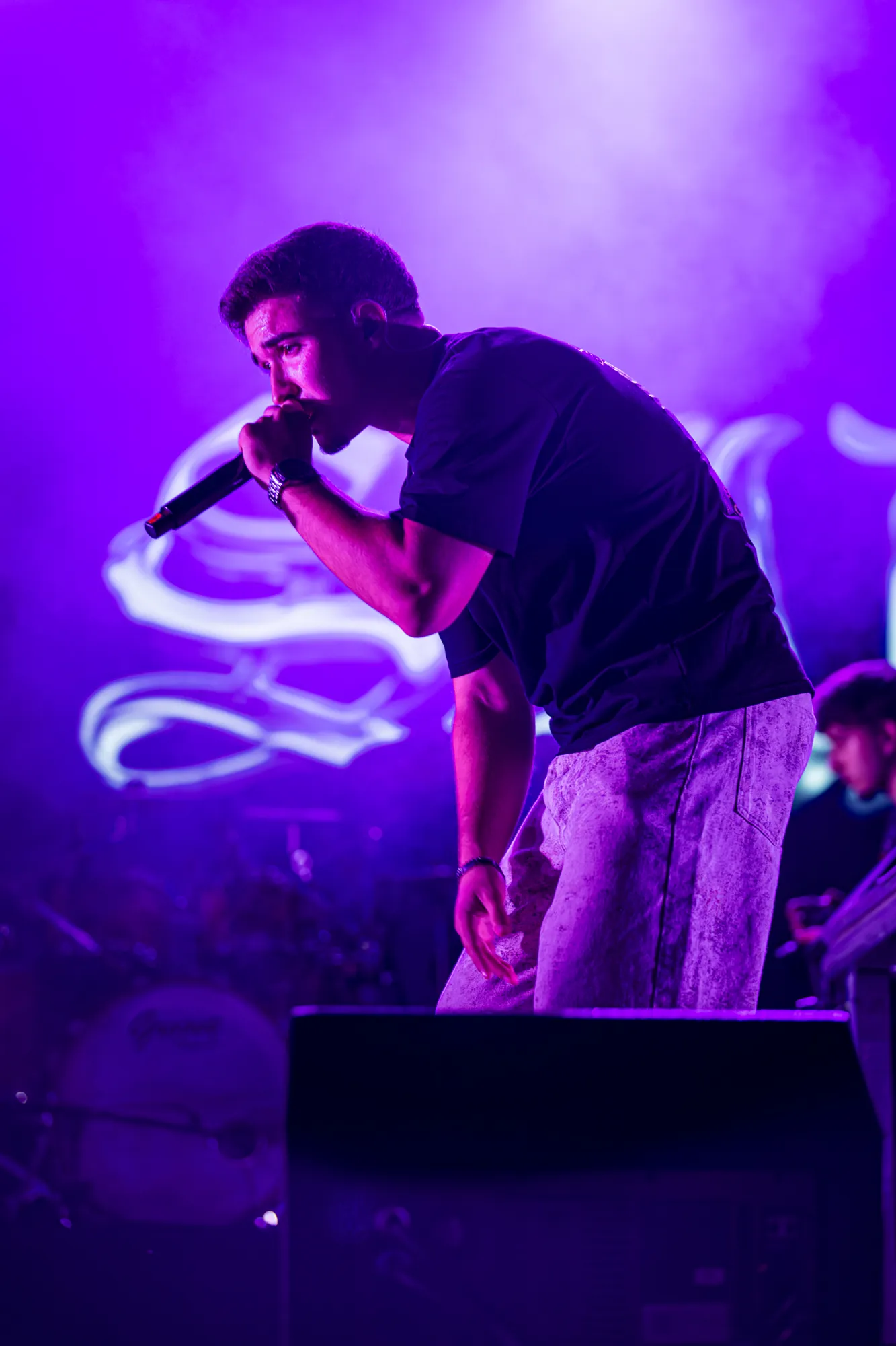 Rapper inclina-se para o público com o microfone, sob luz roxa