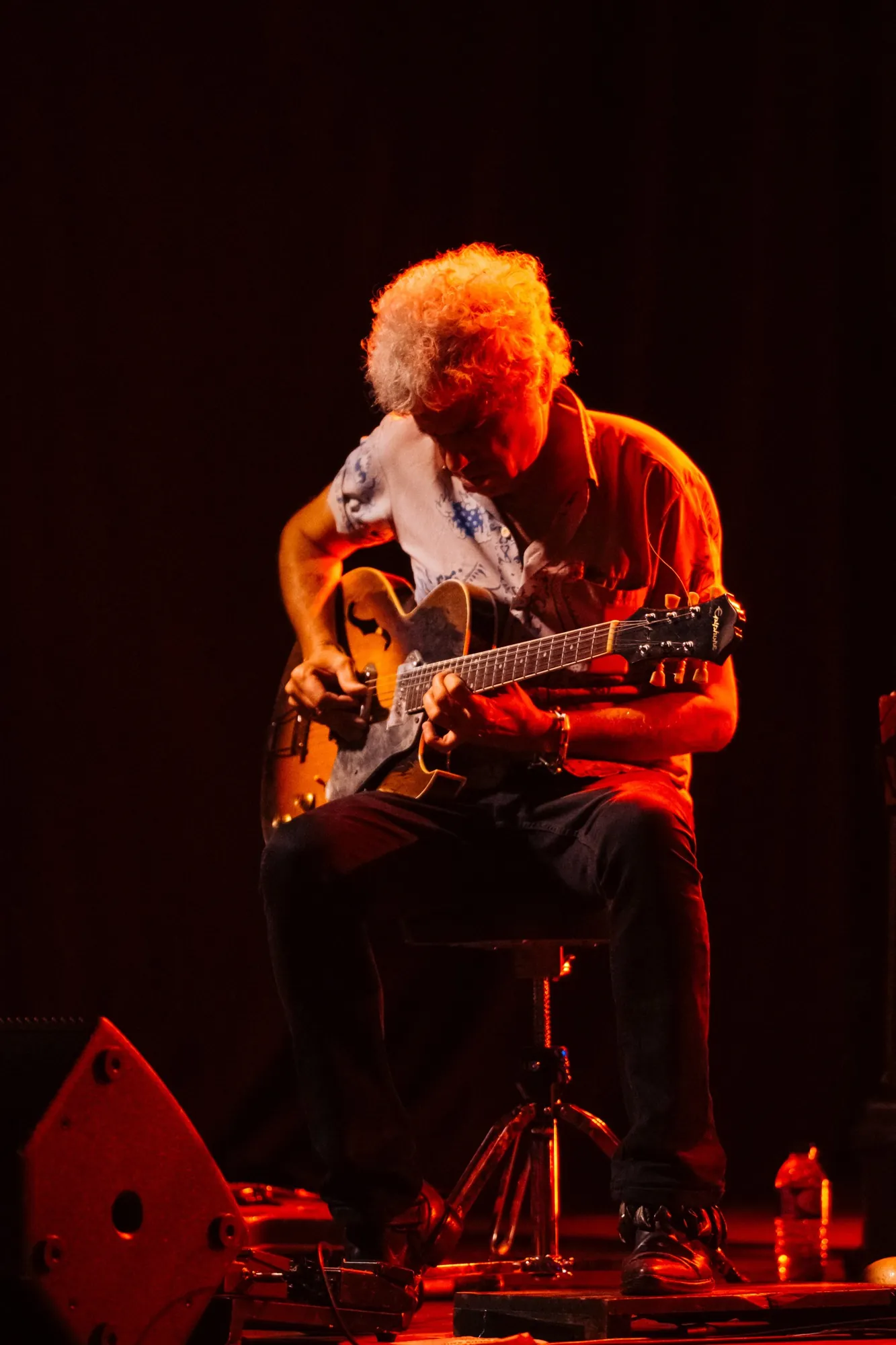 Guitarrista de blues toca sentado, iluminado por luz quente vermelha